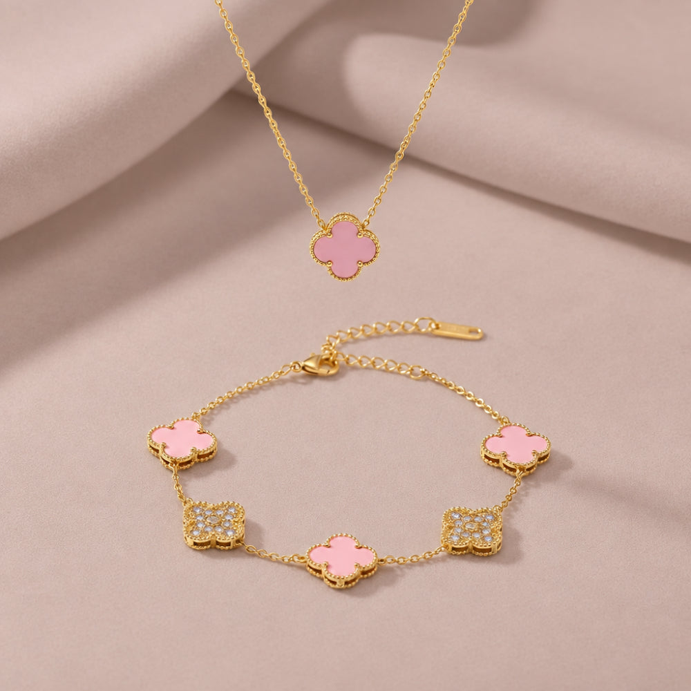 Pink clover pendant on a gold chain with gold bracelet with pink and gold clover charm details. On a pale pink fabric