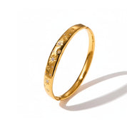 A polished gold bangle bracelet with engraved floral star patterns and small clear stones, shown on a clean white background with a soft shadow.
