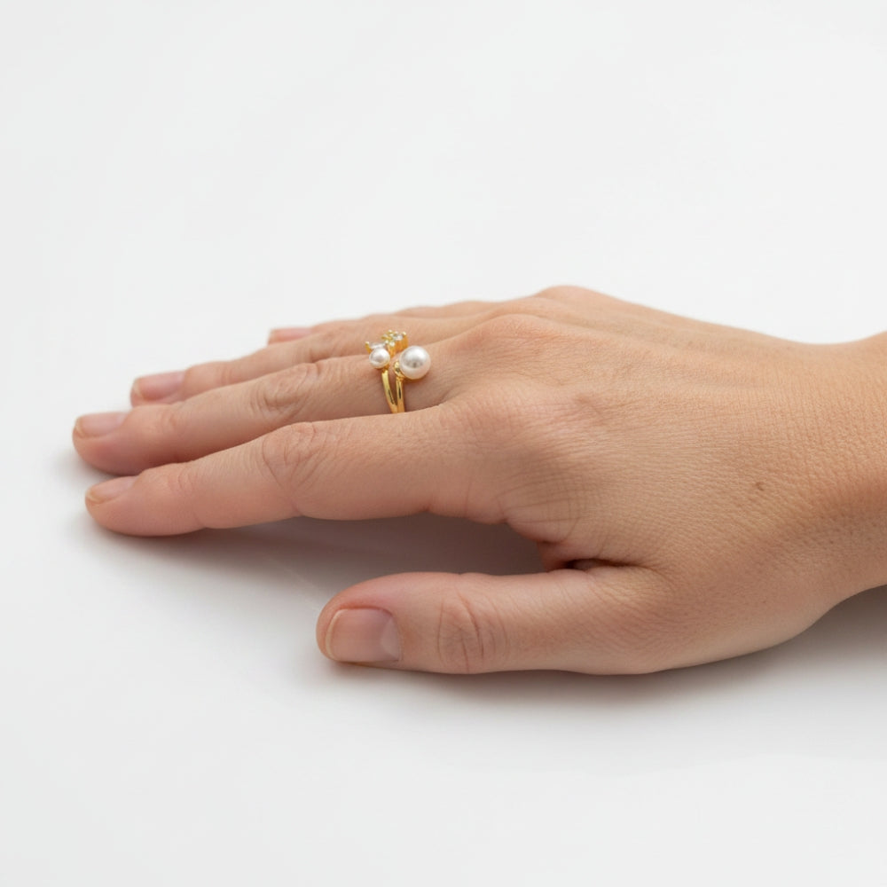 A gold ring with a white pearl and small clear stones, worn on a person's finger against a plain white background.