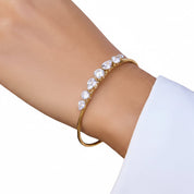 A gold-toned bangle bracelet with five clear teardrop-shaped gemstones, shown worn on a person's wrist against a white background.