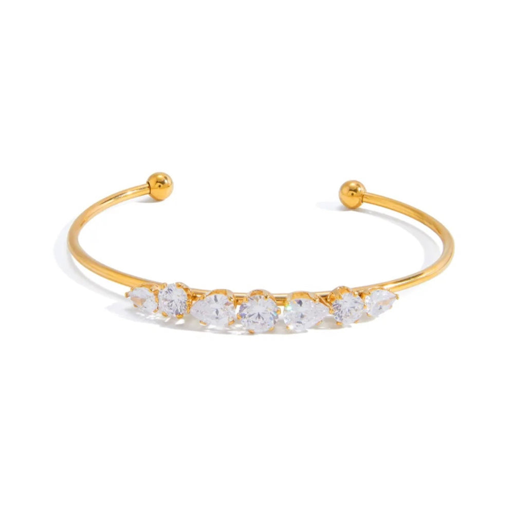 A gold open cuff bracelet featuring a row of clear round-cut gemstones across the front, displayed on a clean white background.