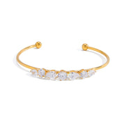 A gold open cuff bracelet featuring a row of clear round-cut gemstones across the front, displayed on a clean white background.