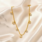 A gold-toned beaded necklace with alternating star and round crystal charms, displayed on draped cream satin fabric.