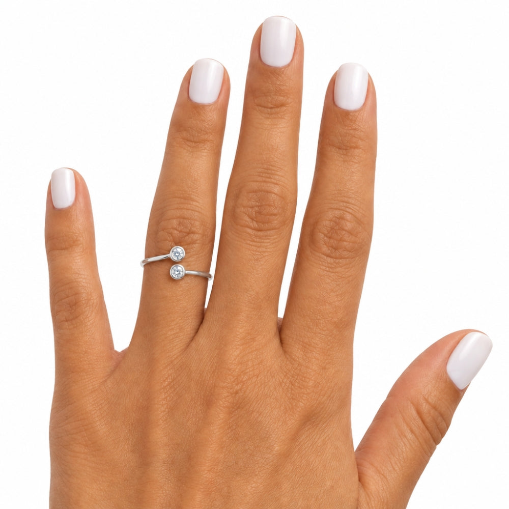 A close-up of a hand with white manicured nails wearing a silver ring with two small round-cut clear gemstones, set against a plain white background.