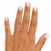 A close-up of a hand with white manicured nails wearing a silver ring with two small round-cut clear gemstones, set against a plain white background.