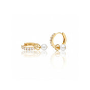 A pair of gold huggie hoop earrings, one adorned with a row of clear pavé stones and the other with a single white pearl dangling from a small gold loop, set against a clean white background with a soft reflection.