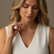 A close-up of a woman wearing a delicate silver necklace with small clear gemstones, styled with a white sleeveless top against a warm, neutral background.