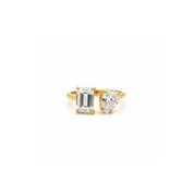 A gold ring featuring an emerald-cut clear gemstone and a pear-cut clear gemstone, photographed on a solid white background.