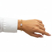 A gold beaded bracelet with a central rectangle -cut clear gemstone, shown worn on a person's wrist against a white background.
