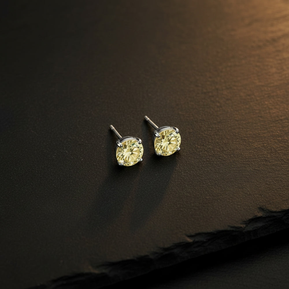 A pair of round-cut yellow gemstone stud earrings in a silver-toned setting, displayed on a dark textured slate surface.