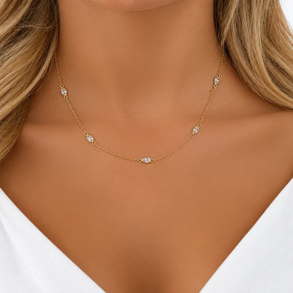 Close up of a gold teardrop crystal necklace worn at the collarbone of a woman 