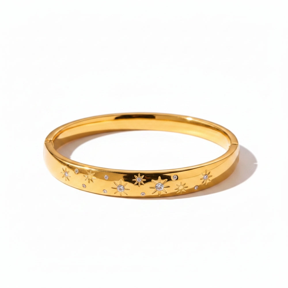 A polished gold bangle bracelet with engraved star motifs and small clear gemstone accents, displayed on a clean white background.