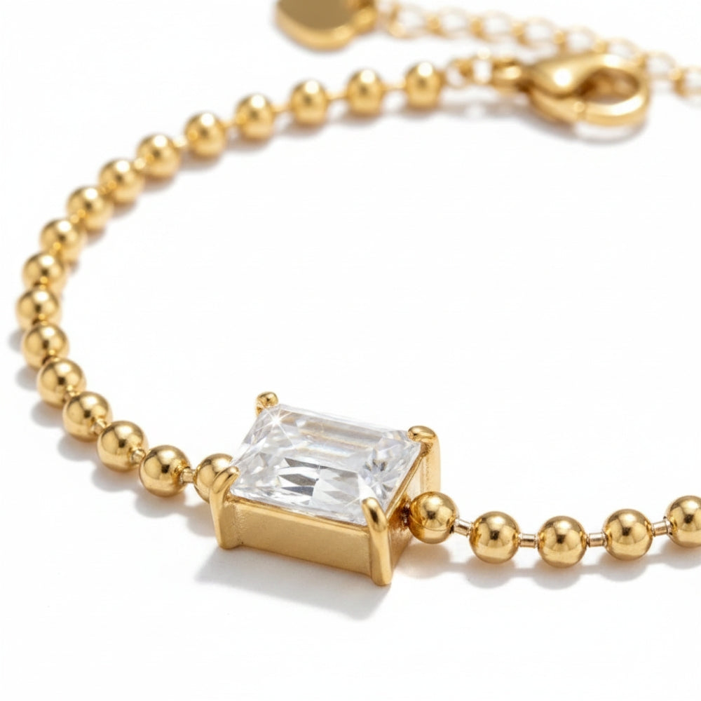 A gold beaded bracelet featuring a rectangular clear gemstone pendant in a gold bezel setting, shown on a clean white background.