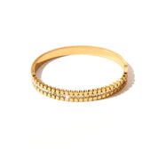 A gold-plated bangle bracelet featuring a textured beaded outer band and a central channel set with small clear stones, shown on a plain white background.