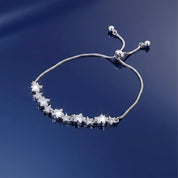 A silver-toned adjustable cord bracelet featuring a row of clear star-shaped crystal charms, displayed on a reflective dark blue surface.