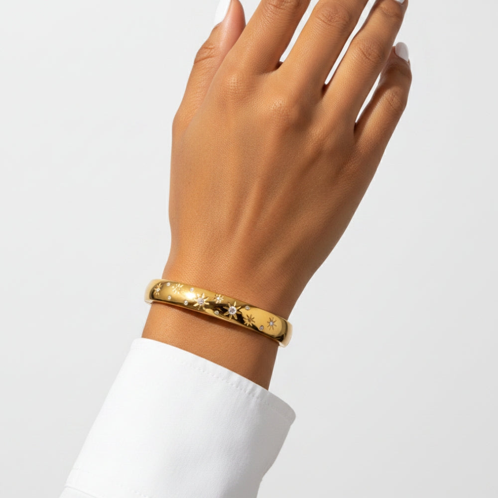A gold bangle bracelet with a star pattern, worn on a person's wrist against a clean white background.