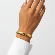 A gold bangle bracelet with a star pattern, worn on a person's wrist against a clean white background.