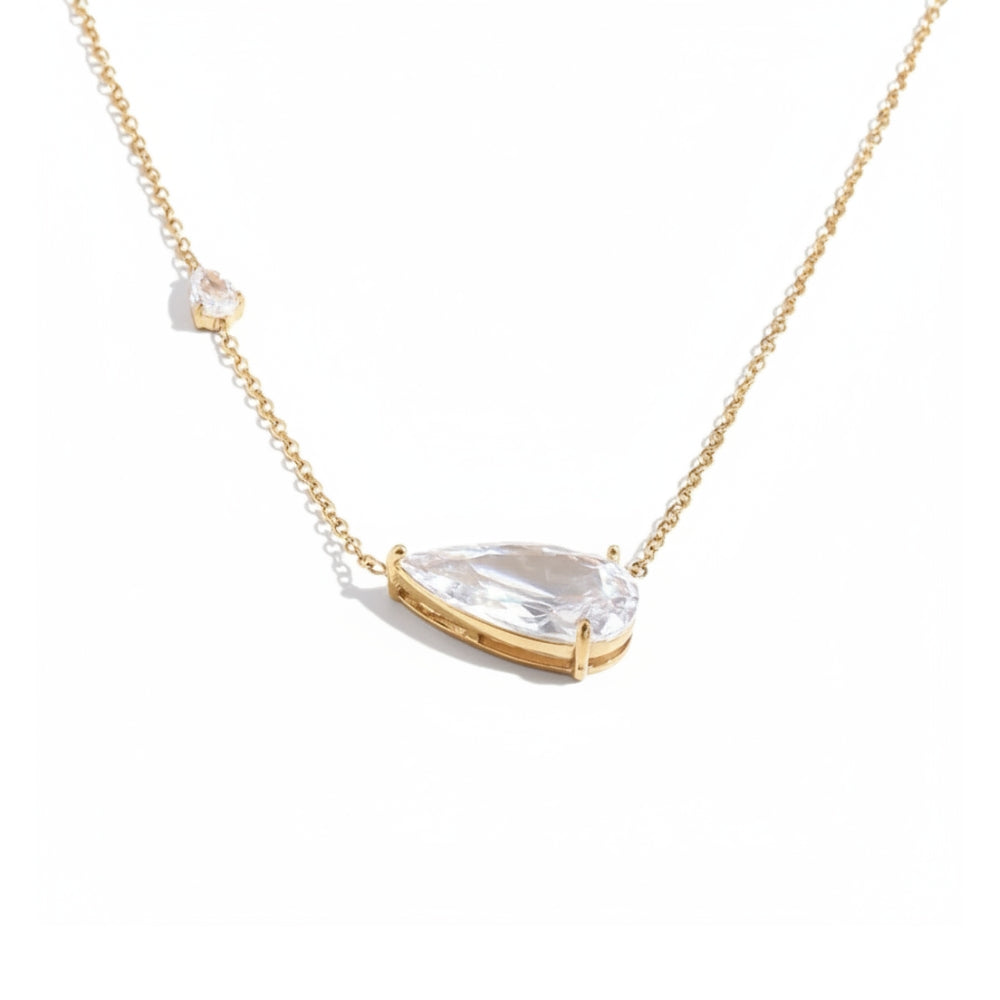 A delicate gold chain necklace featuring a large teardrop-shaped clear gemstone pendant in a gold bezel setting, with a smaller accent gemstone on the chain, shown against a solid white background.