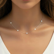 A close-up of a model wearing a delicate silver star necklace with five small star charms spaced along a fine chain.