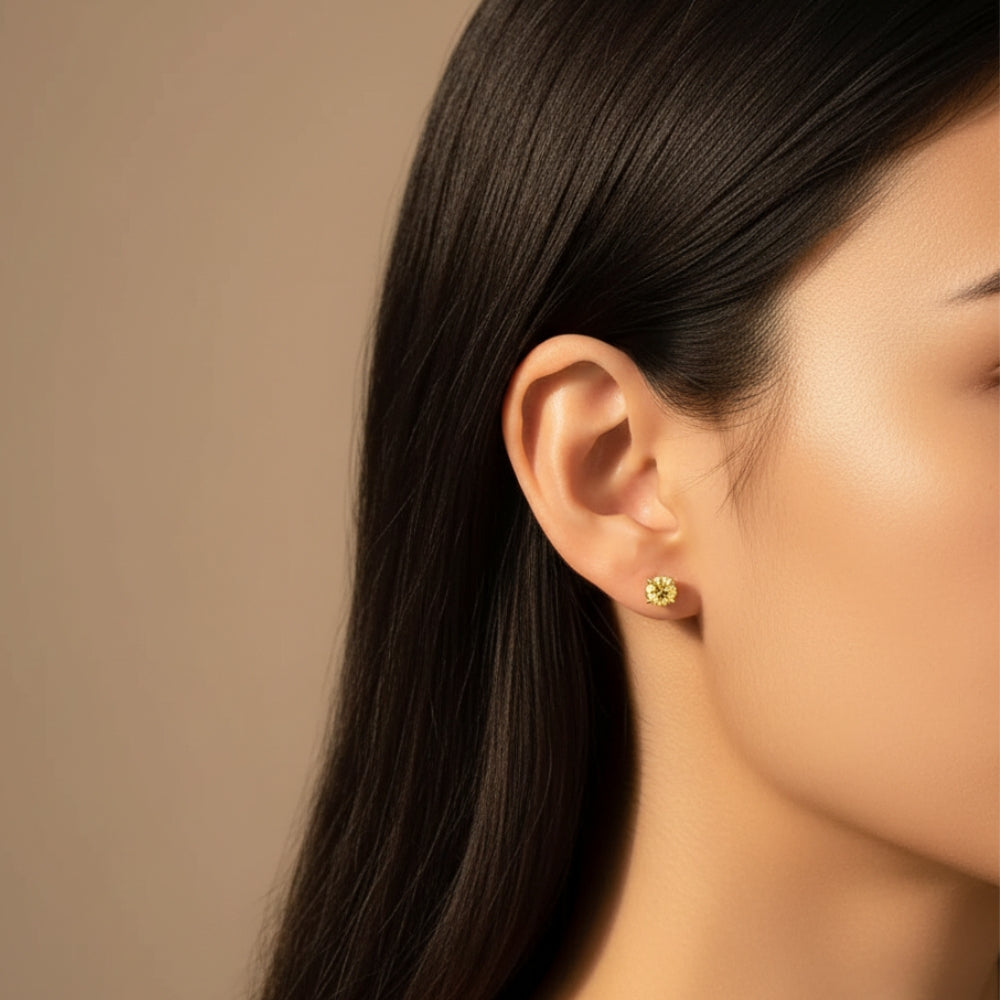 A close-up side profile of a woman with long dark hair wearing a small silver stud earring with a yellow stone. 