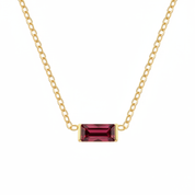 A gold chain necklace featuring a rectangular emerald-cut dark red gemstone pendant, shown against a plain white background.