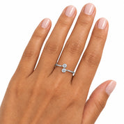 A close-up of a hand wearing a slim silver ring with two small clear gemstones, shown against a plain white background.