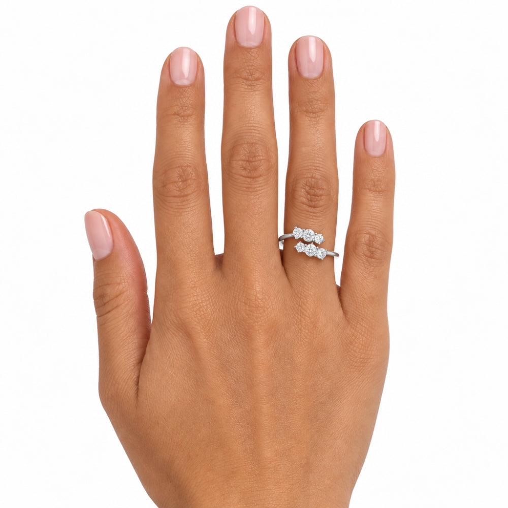 A close-up of a hand with light pink manicured nails wearing a silver ring with three small round-cut clear gemstones, set against a plain white background.