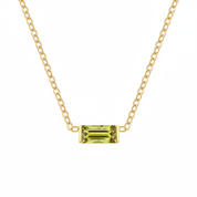 A delicate yellow gold chain necklace featuring a small rectangular emerald-cut olive green gemstone pendant, displayed against a solid white background.