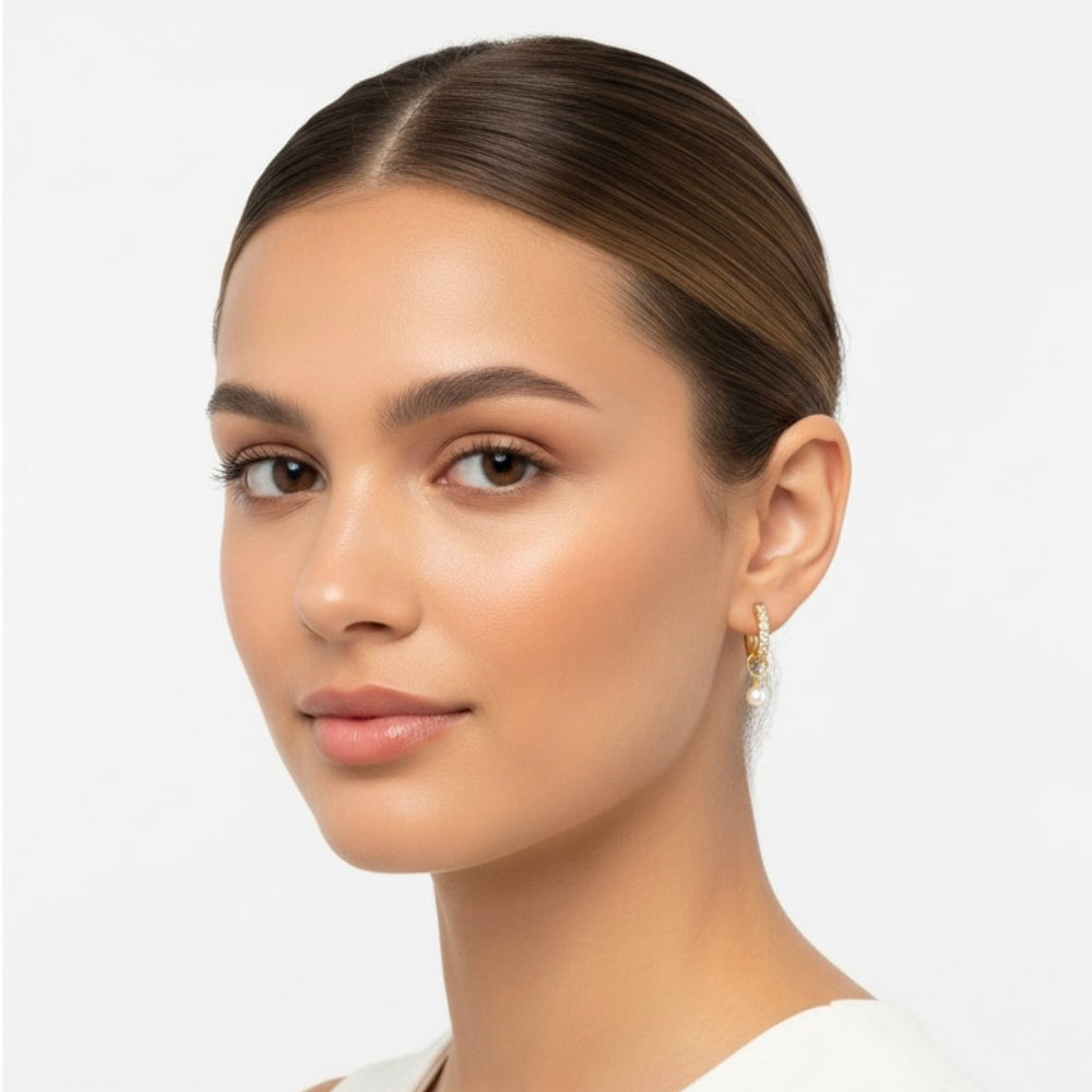 A close-up portrait of a woman with her hair pulled back, wearing a delicate gold hoop earring with a small white pearl drop, set against a clean light gray background.