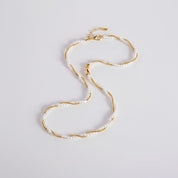A delicate double-strand necklace featuring small white faux pearls and twisted gold-tone metal, laid out in an S-shape on a clean white background.