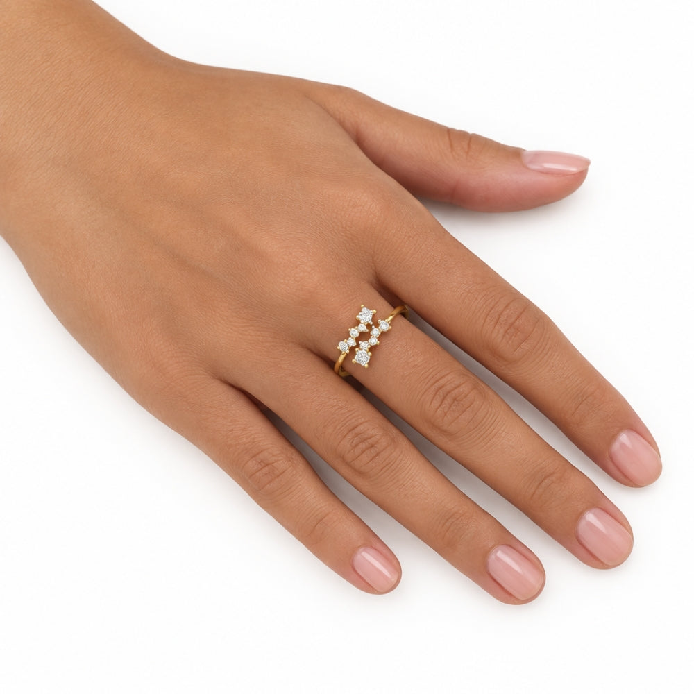 A gold ring with three small white gemstones set in a row, worn on the ring finger of a hand with light pink manicured nails, against a plain white background.