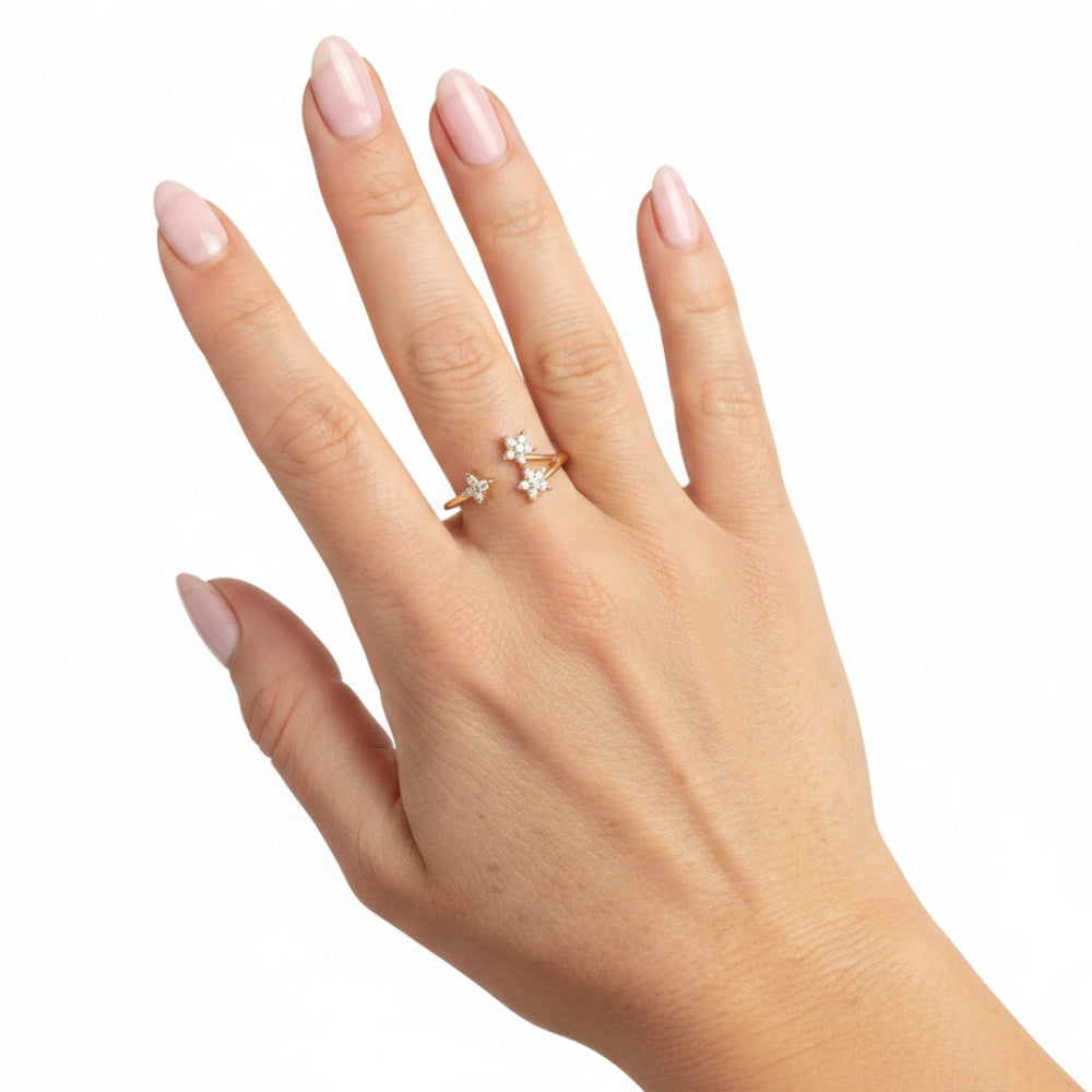 A hand with pale pink manicured nails wearing a delicate gold ring with three small star-shaped clear gemstone clusters, set against a plain white background.
