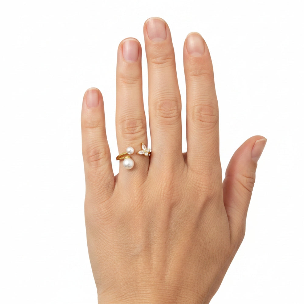 A gold ring with two white pearls and a small white flower detail, shown worn on a person's ring finger against a plain white background.