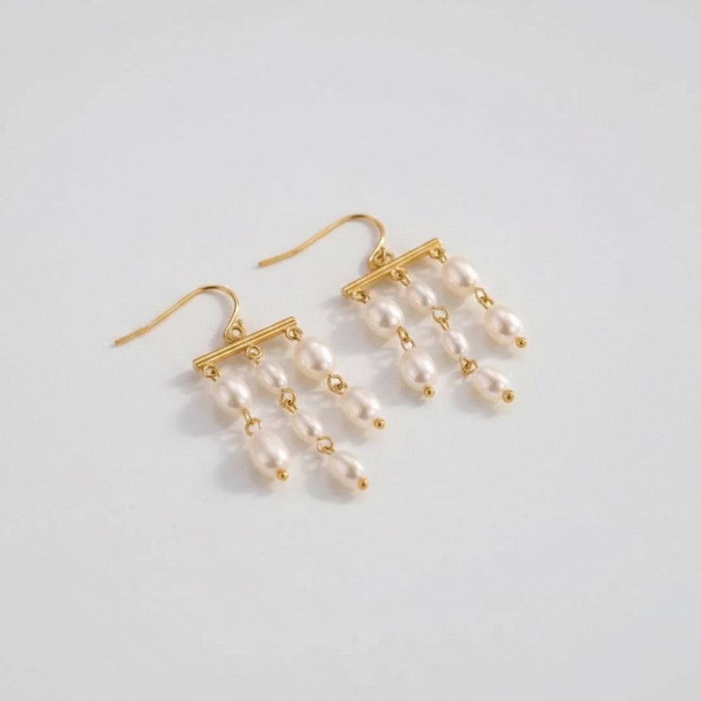A pair of gold dangle earrings with white pearl-like beads, displayed on a clean light gray background.