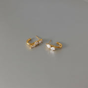 A pair of gold hoop earrings with clear crystals, displayed on a neutral gray background.
