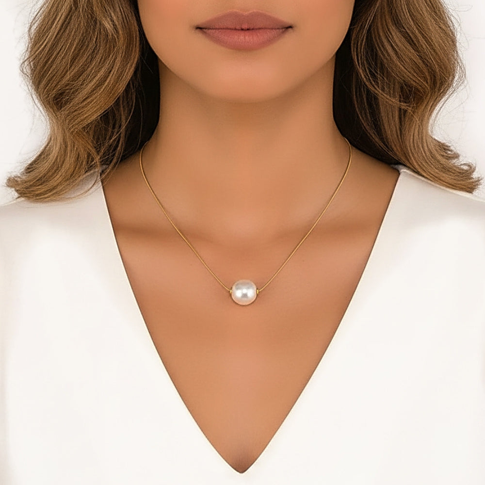 A close-up of a woman wearing a delicate gold chain necklace with a single lustrous white pearl pendant, styled with a white V-neck top against a clean white background.
