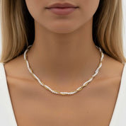 A close-up of a woman wearing a delicate twisted necklace made of white pearls and small gold accents, shown against her neck and shoulders.