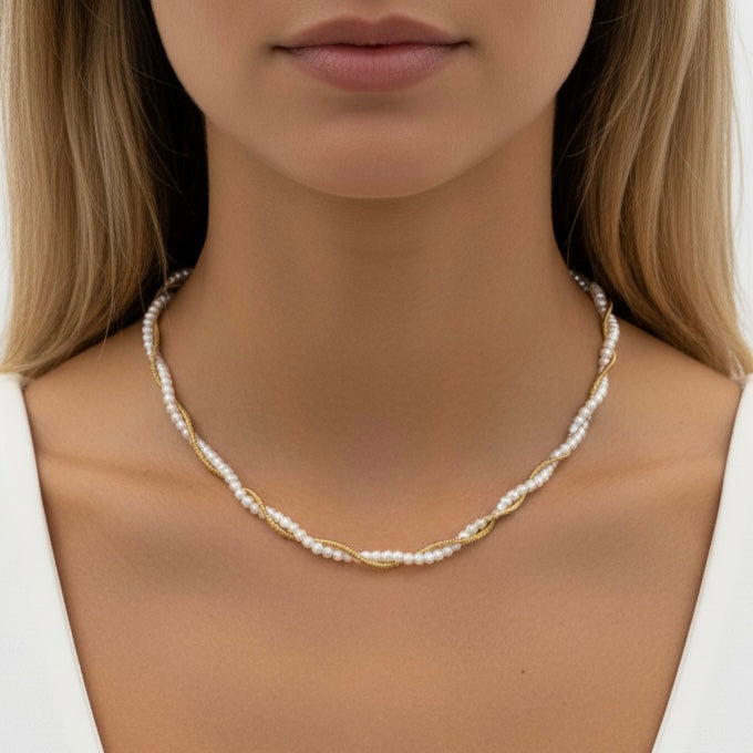 A close-up of a woman wearing a delicate twisted necklace made of white pearls and small gold accents, shown against her neck and shoulders.