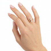 A close-up of a hand with light pink manicured nails wearing a gold ring with three small clear gemstones, set against a plain white background.