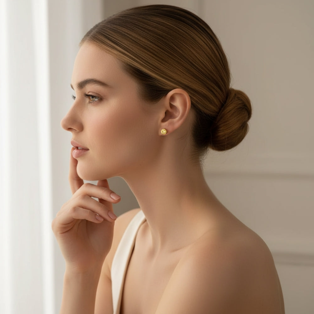 A woman in profile wearing a small lemon stud earring, with her hair styled in a low bun and a neutral indoor background.
