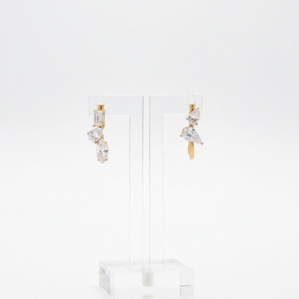 A pair of gold drop earrings with clear marquise and baguette-cut stones, displayed on a clear acrylic stand against a white background.