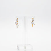 A pair of gold drop earrings with clear marquise and baguette-cut stones, displayed on a clear acrylic stand against a white background.