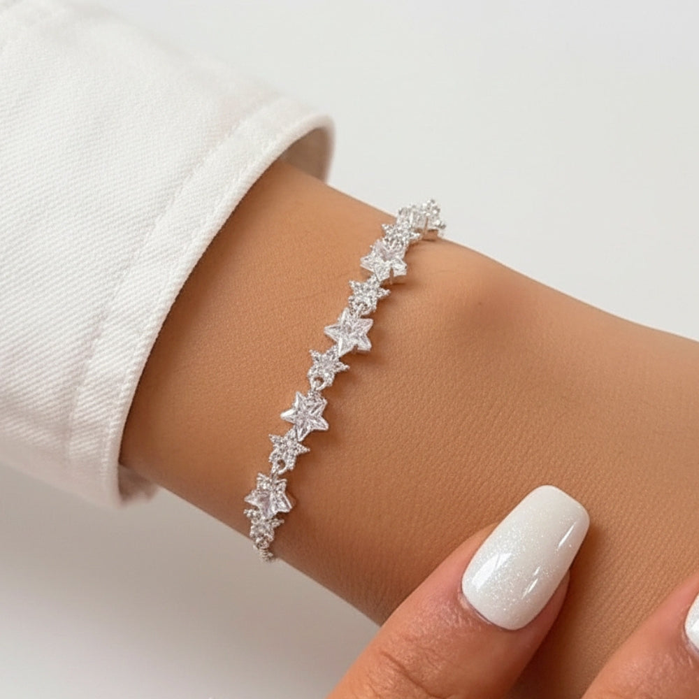 A close-up of a delicate silver bracelet with a row of small star-shaped clear gemstones worn on a person's wrist, with a white sleeve and manicured nails visible.