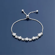 A silver adjustable slide bracelet featuring a row of star-shaped clear gemstones, displayed on a dark blue reflective surface.