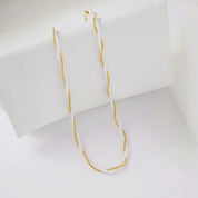A delicate necklace featuring white freshwater pearls and a twisted gold-tone metal core, draped over a white display block.