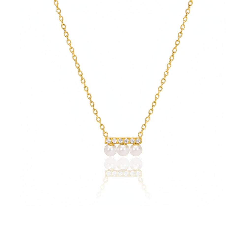 A delicate gold chain necklace featuring a small horizontal bar with three white pearls and tiny clear stones, displayed on a clean white background with a soft reflection below.