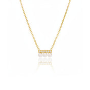 A delicate gold chain necklace featuring a small horizontal bar with three white pearls and tiny clear stones, displayed on a clean white background with a soft reflection below.