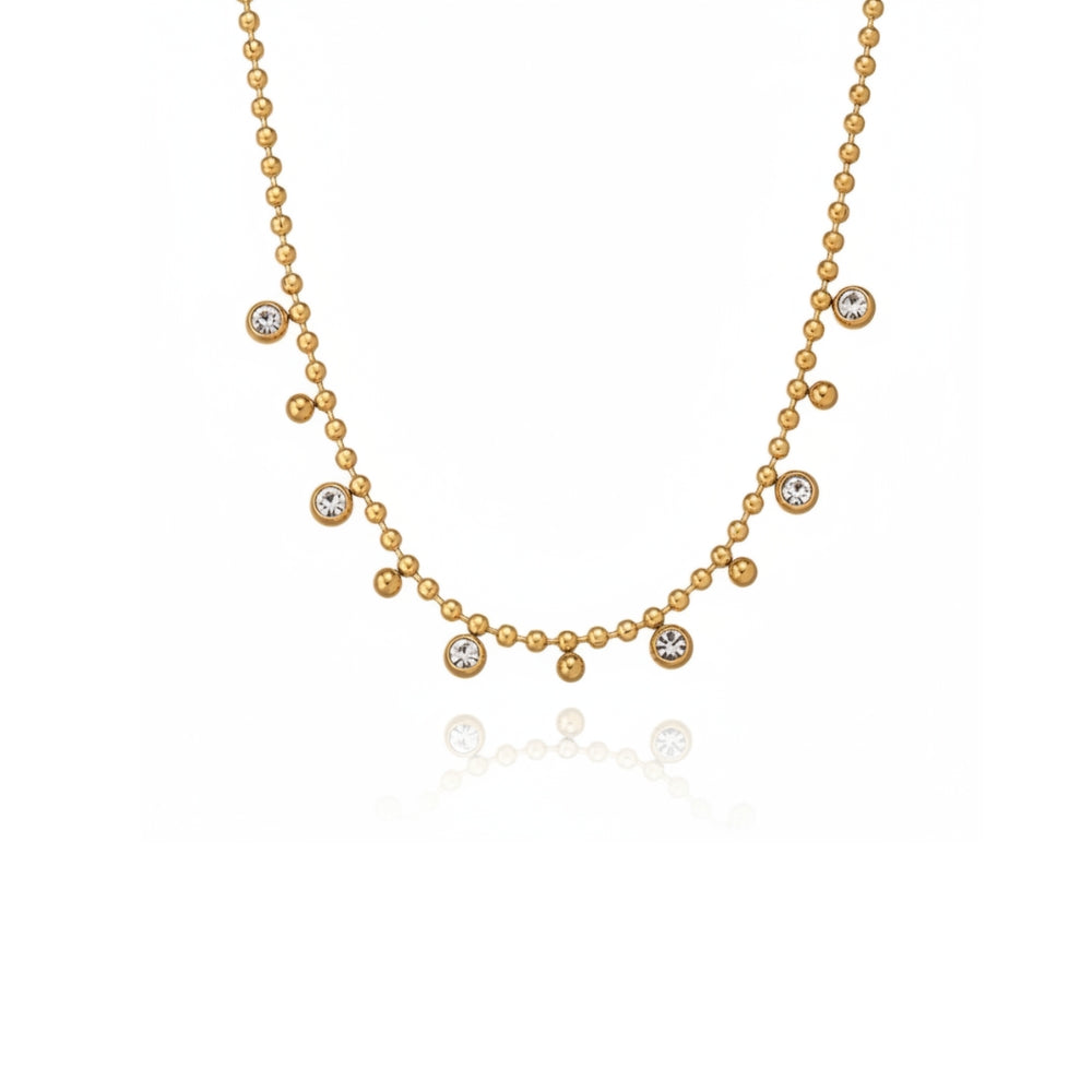 A delicate gold necklace featuring a beaded chain with six small round bezel-set clear stones arranged in a gentle arc, displayed on a clean white background with a soft reflection below.