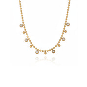 A delicate gold necklace featuring a beaded chain with six small round bezel-set clear stones arranged in a gentle arc, displayed on a clean white background with a soft reflection below.