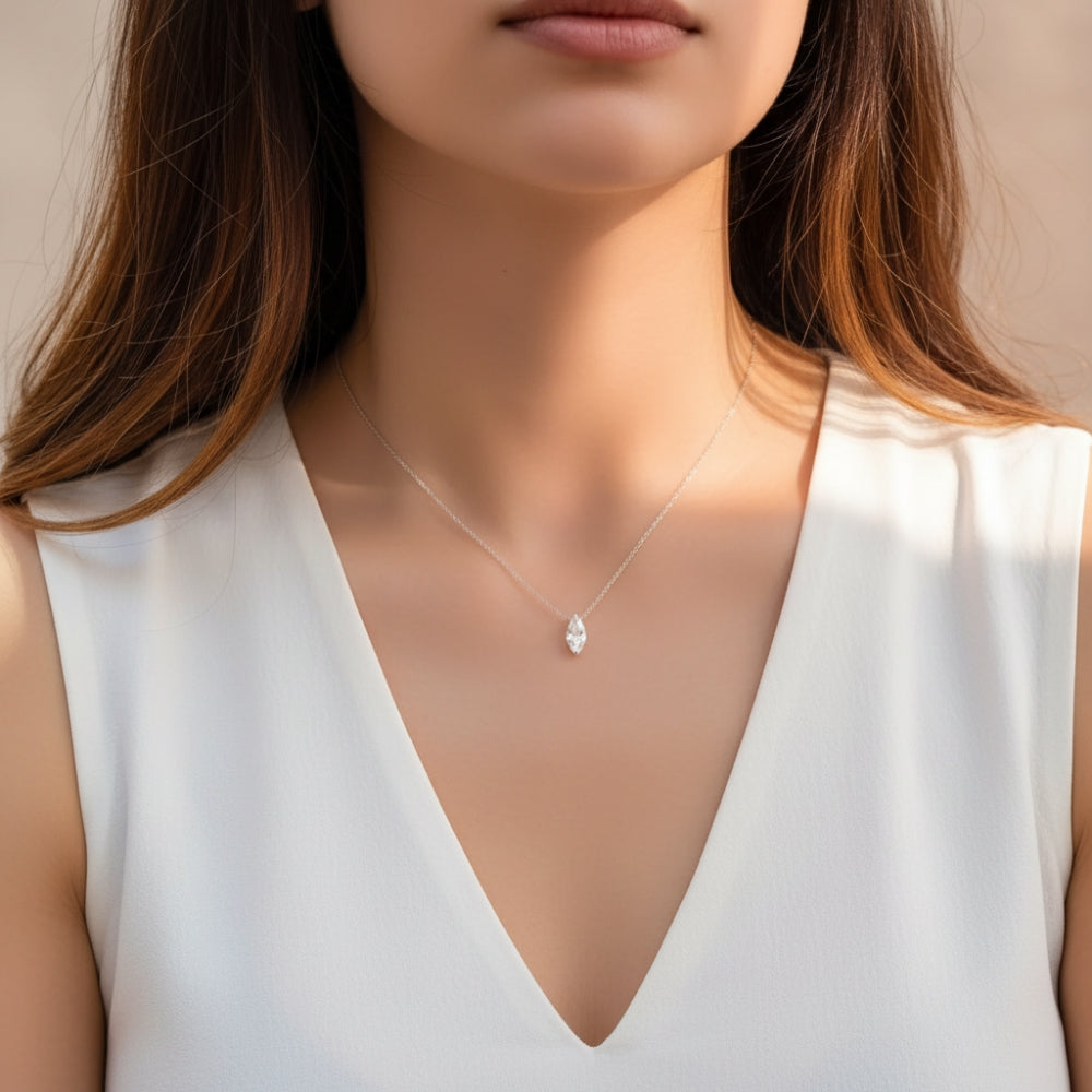 A close-up of a woman wearing a delicate silver chain necklace with a small teardrop-shaped clear gemstone pendant, paired with a white sleeveless V-neck top.